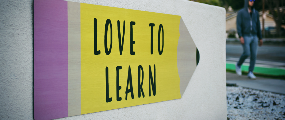 Placa em formato de lpis, escrito "Love To Learn" grudado na parede