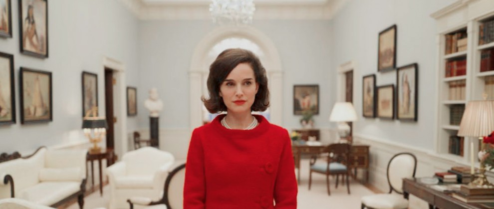 Natalie Portman, caracterizando a primeira dama Jckie, em um vestido vermelho e um corte curto dentro da Casa Branca