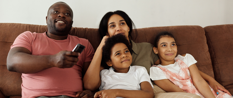Pai, me e filhos sentados no sof assistindo a um filme e rindo.