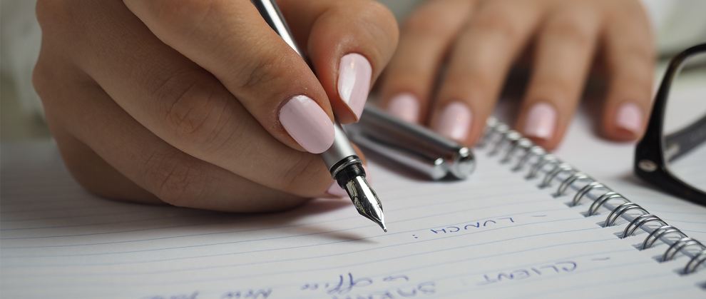 Imagem de uma mo escrevendo no caderno com uma caneta