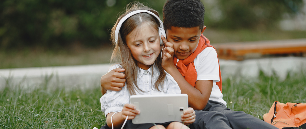 Uma menininha com o seu colega escutando música e mexendo no tablet.