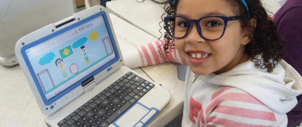Menina sorrindo ao mesmo tempo fazendo uma atividade no computador 