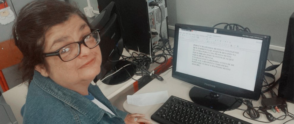 l Professora Cyrene Leite de Almeida de frente a um computador, olhando para a foto